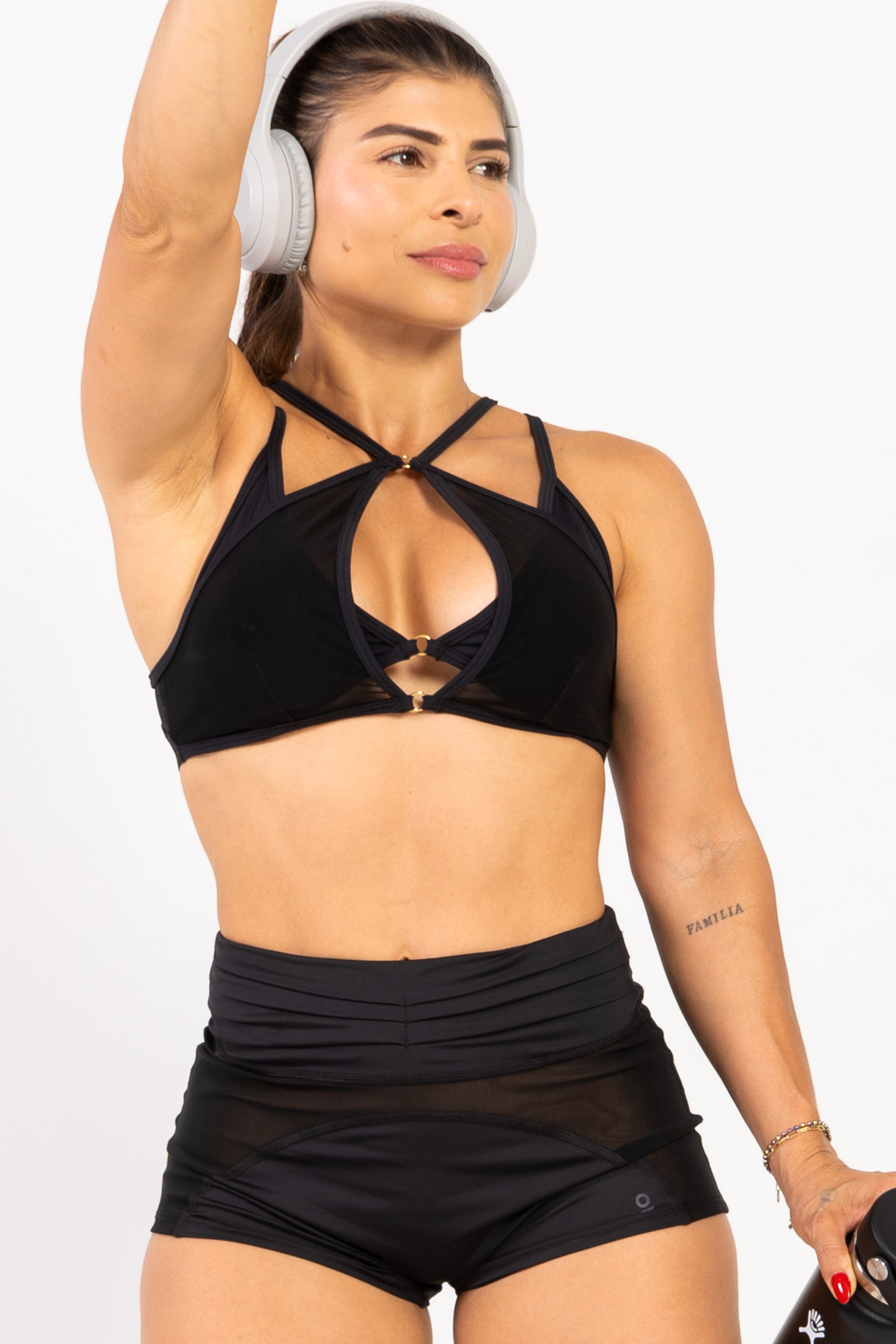 Woman wearing a black sports bra and shorts with white headphones on a plain background 