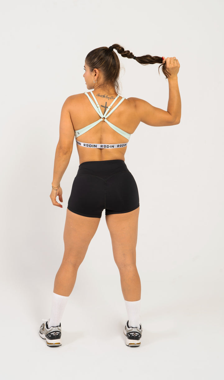 Woman wearing a sports bra and shorts with visible branding on a white background. 