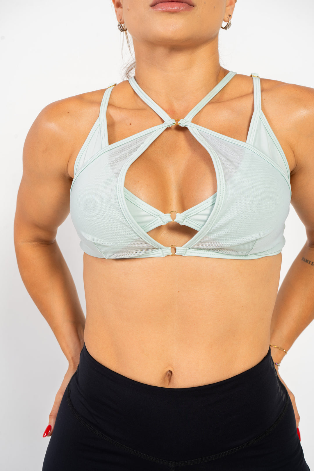 Woman wearing a mint sports bra and black leggings on a white background 