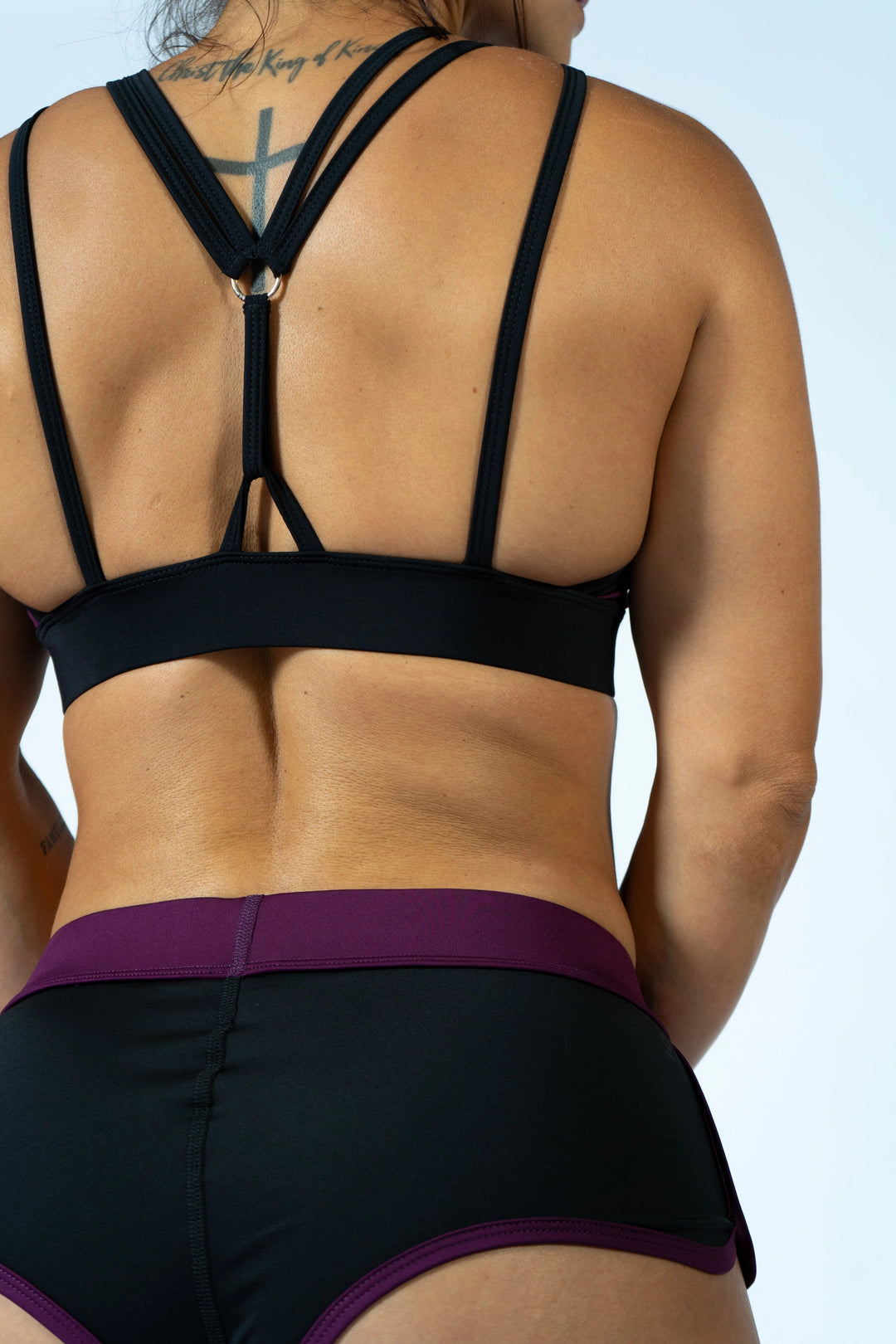 Person wearing a black sports bra and shorts with a purple waistband on a light blue background #color_black-magenta