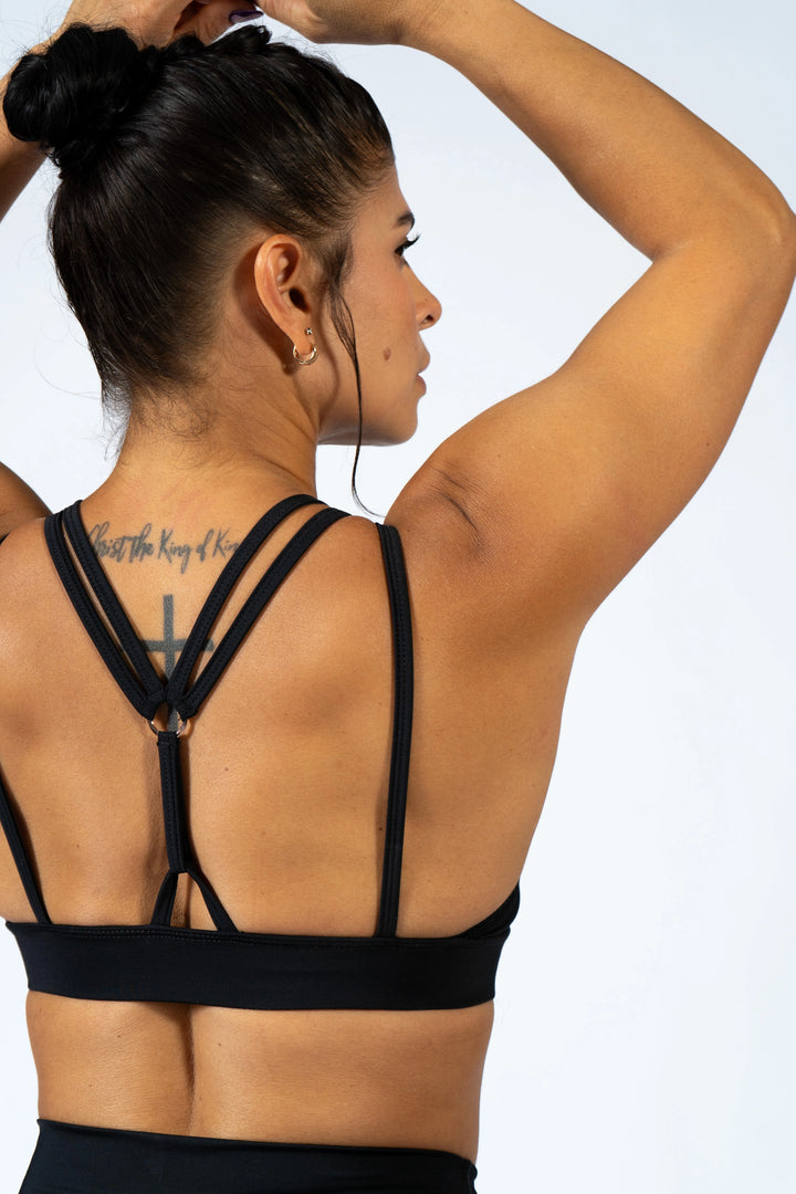 Woman wearing a black sports bra with criss-cross straps on a light gray background #color_black