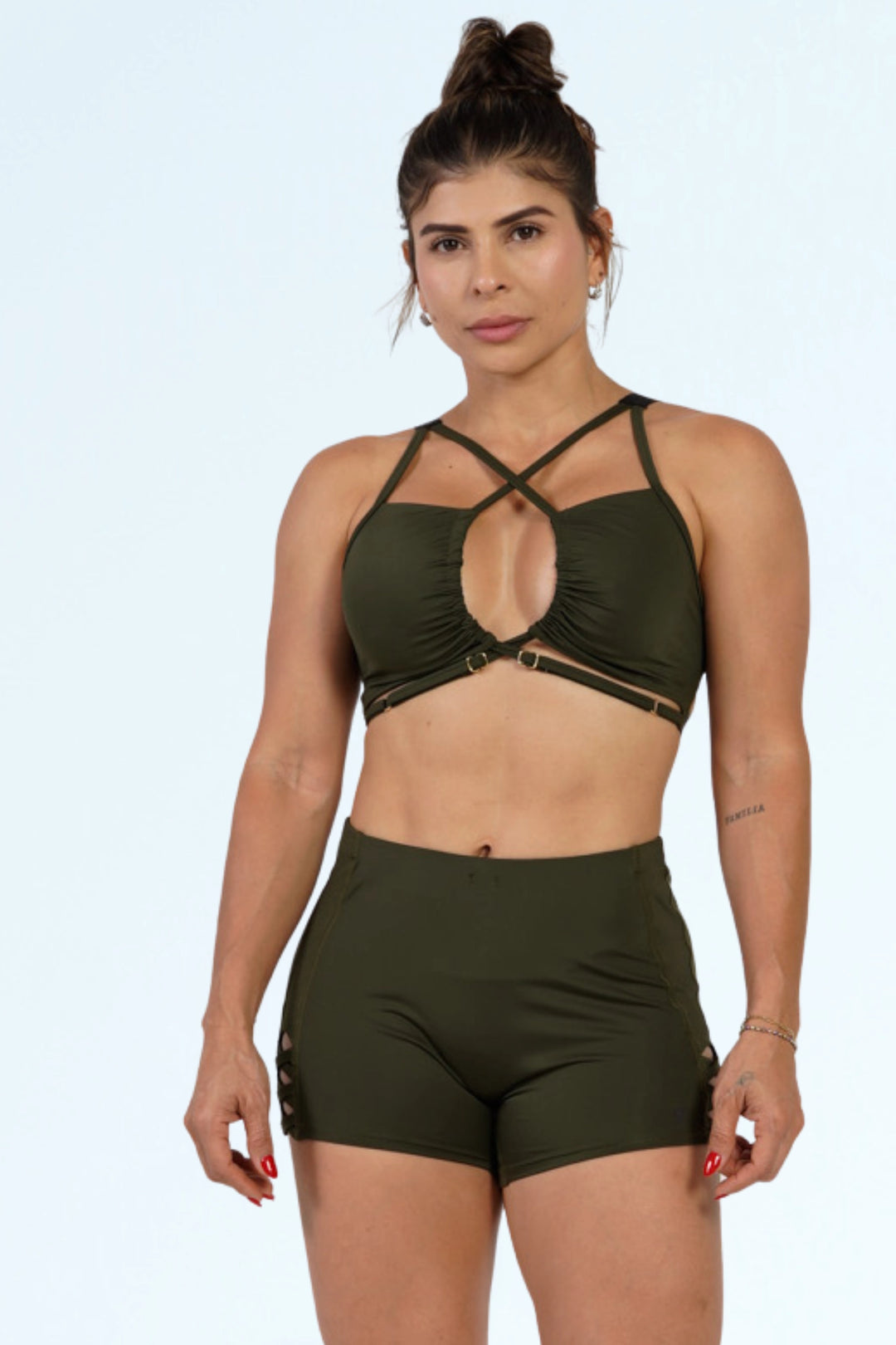 Woman wearing an olive green sports bra and shorts set on a white background #color_riffle-green