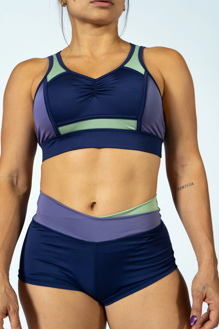 Person wearing a blue and green sports bra and shorts set on a light gray background #color_iris-mystical-basil